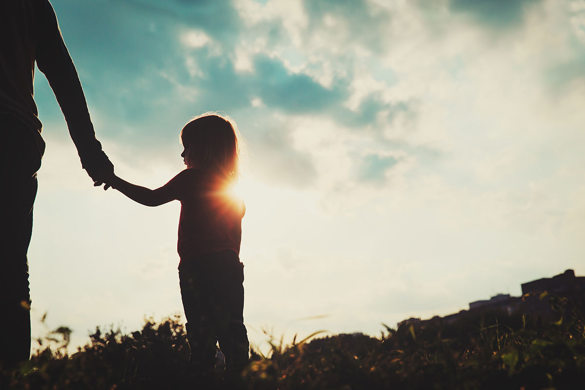parent holding little girl's hand facing the sunset
